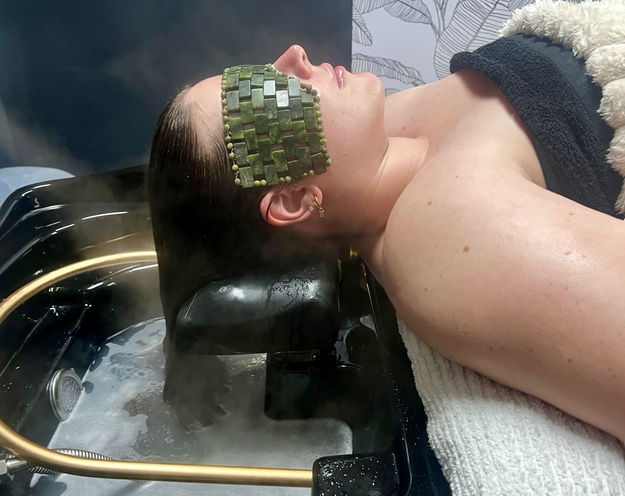 A guest relaxing in the head-spa basin with a jade eye mask and rising steam